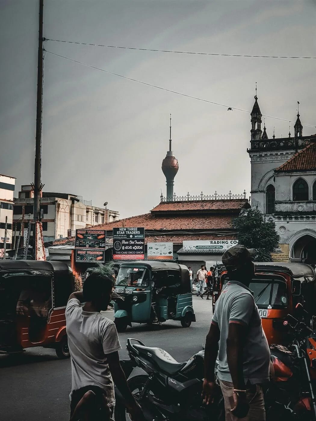 Busy Colombo street scene with tuk-tuks, motorbikes and the Lotus Tower rising above the city - the transport reality that greets every visitor to Sri Lanka