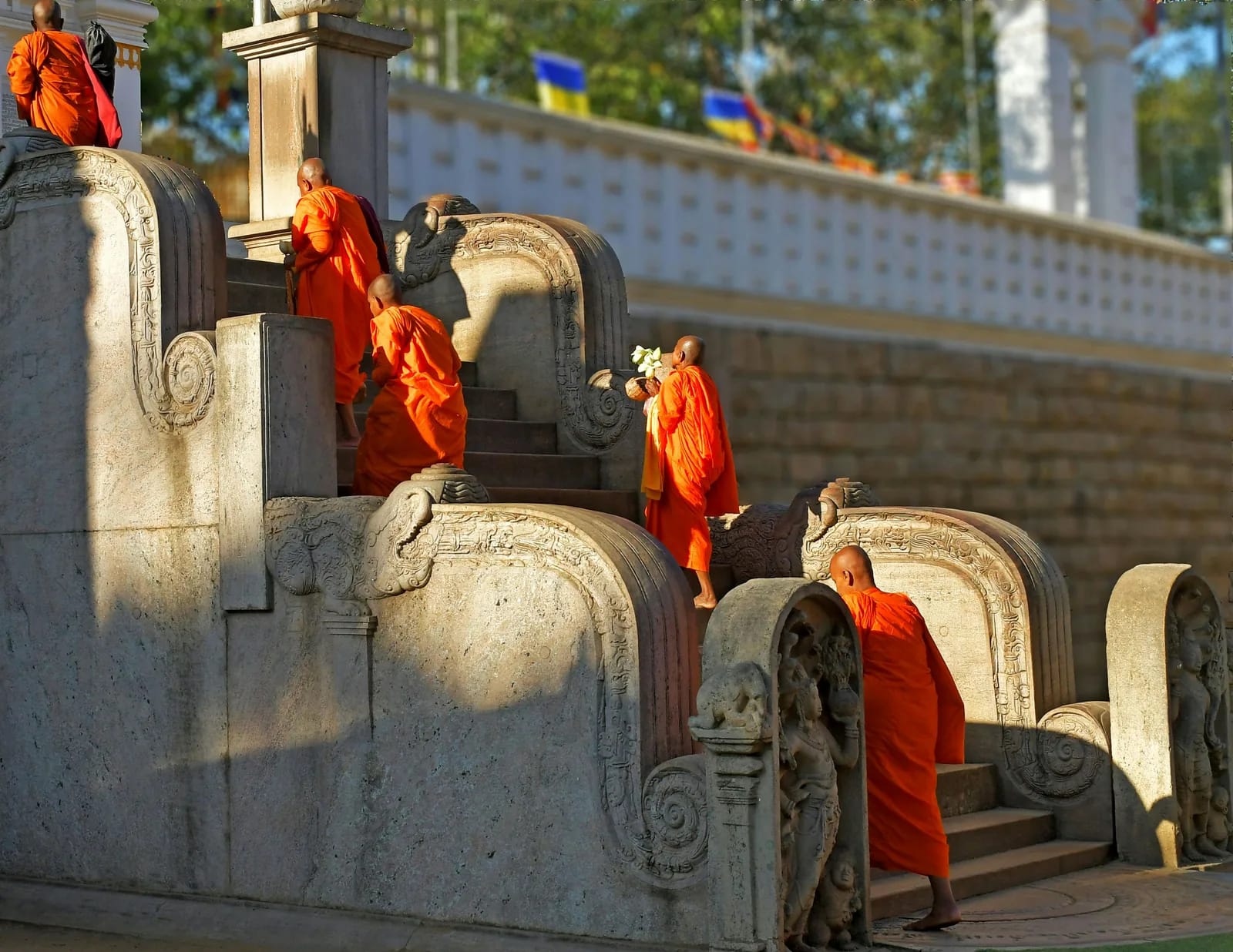 Buddhist monks in saffron robes ascending the ornate carved stone steps of a major Sri Lanka Buddhist temple at golden hour