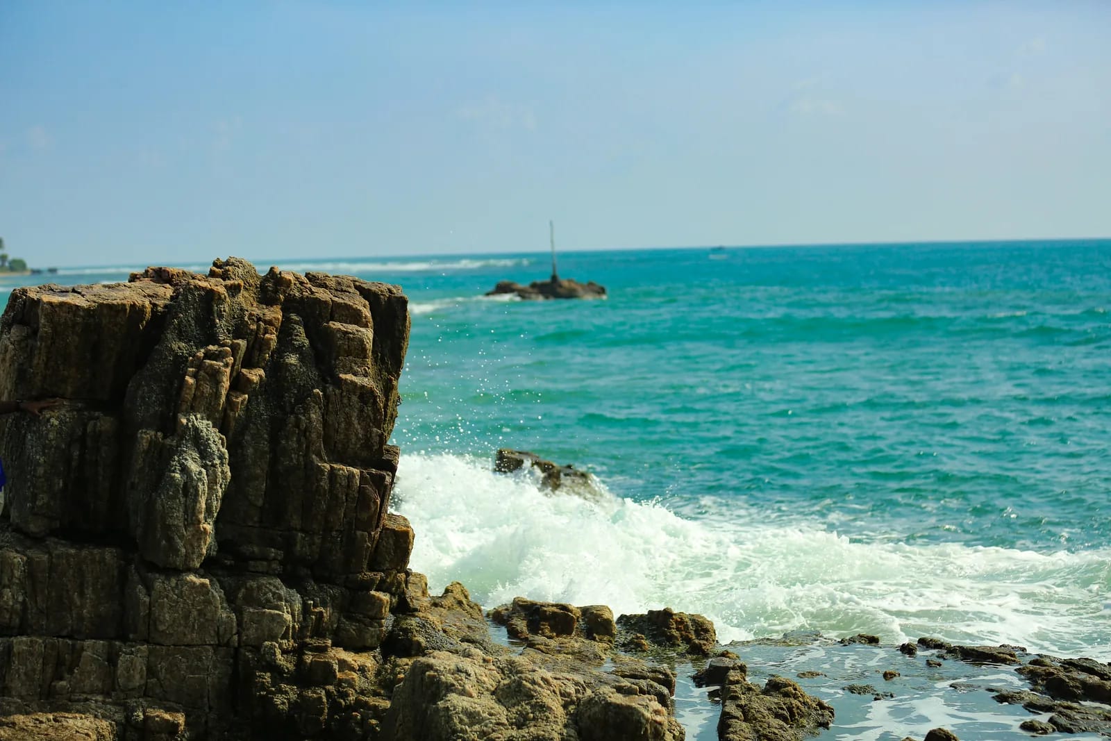 Rocky coastline with turquoise waves crashing against the rugged rocks of Trincomalee's east coast, Sri Lanka