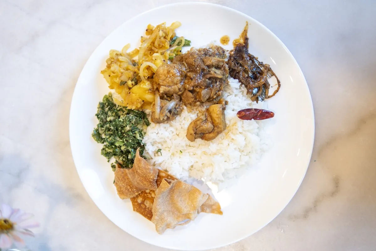A Sri Lankan rice and curry plate with chicken curry, potato, greens and papadums