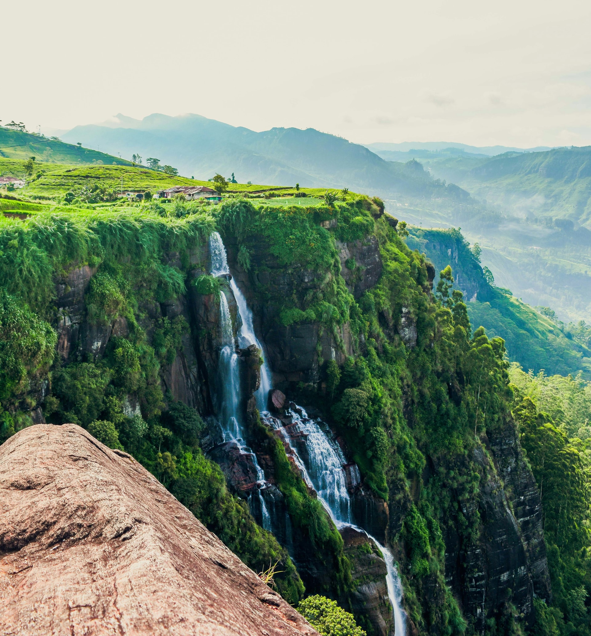 A wide waterfall cascading through the lush green hill country of Sri Lanka's Kandy District — the kind of landscape that surrounds Huluganga Ella on the western slopes of the Knuckles Range