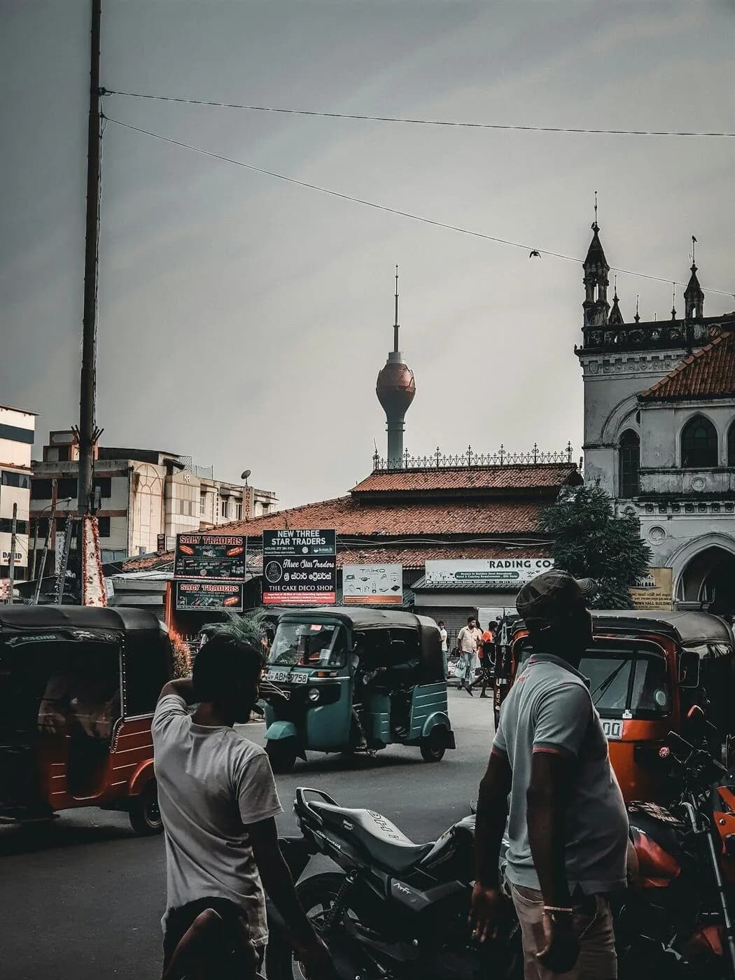 Busy Colombo street scene with tuk-tuks, motorbikes and the Lotus Tower rising above the city - the transport reality that greets every visitor to Sri Lanka