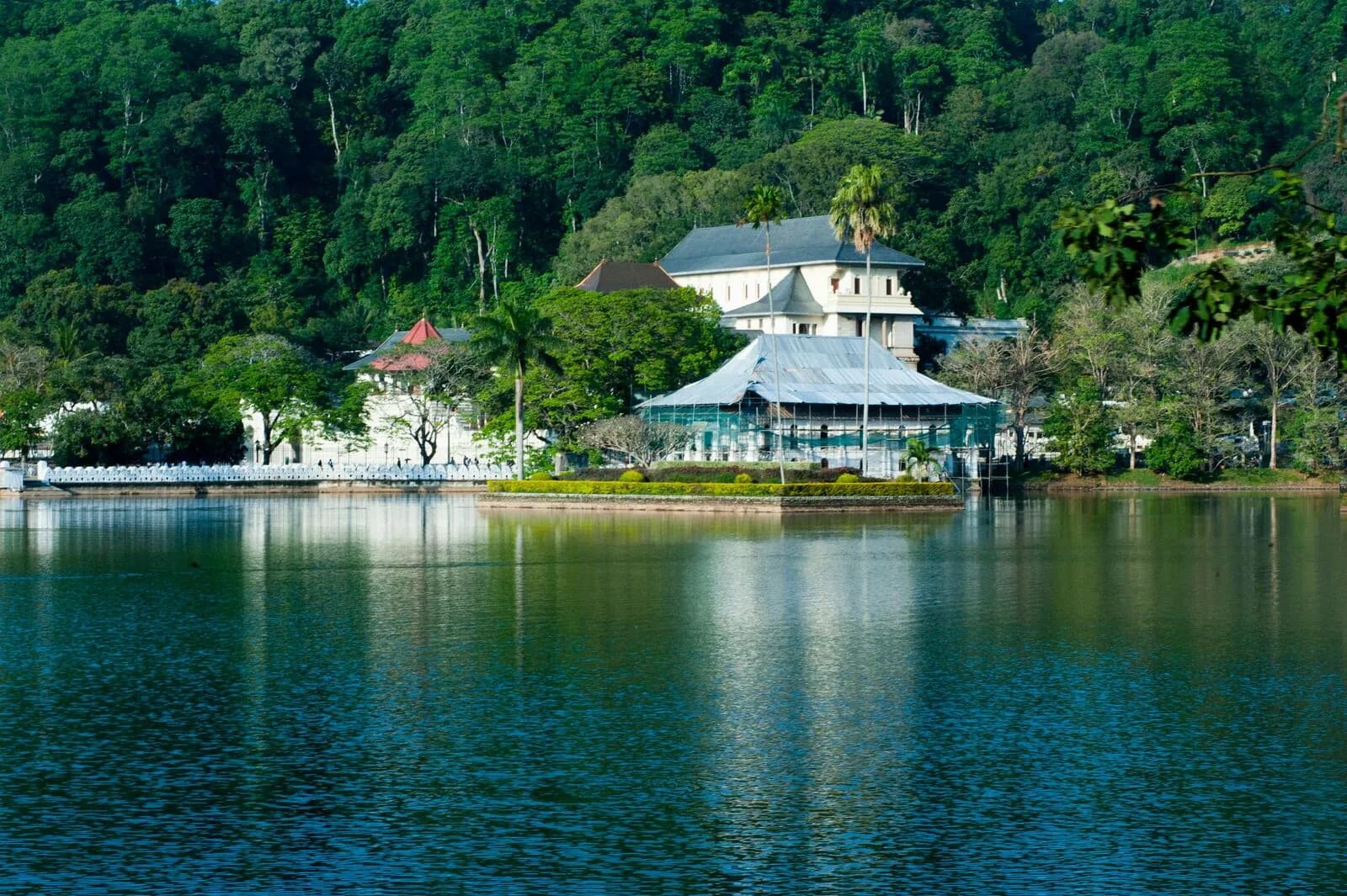 Kandy Lake at dusk with the Temple of the Tooth illuminated in the background, surrounded by forested hills