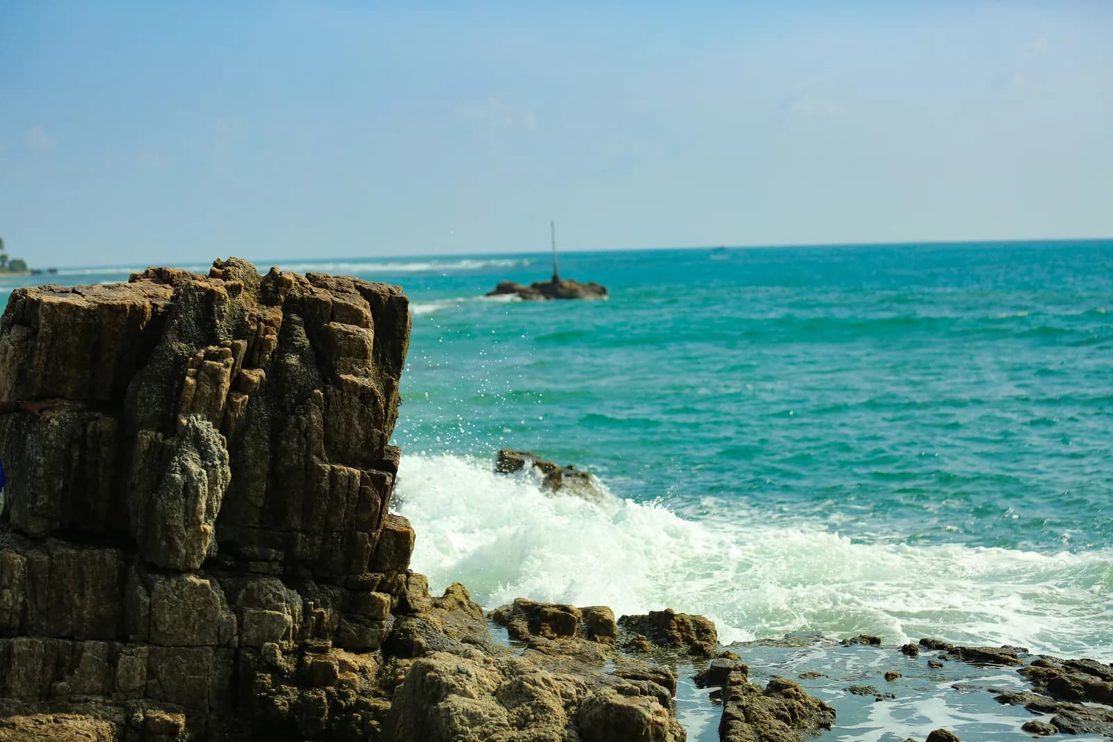 Rocky coastline with turquoise waves crashing against the rugged rocks of Trincomalee's east coast, Sri Lanka
