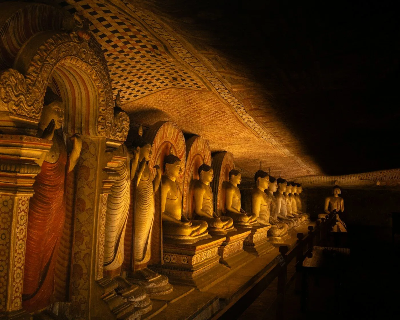 Golden Buddha statues inside the Dambulla Cave Temple, lit by shafts of light through ancient rock ceiling
