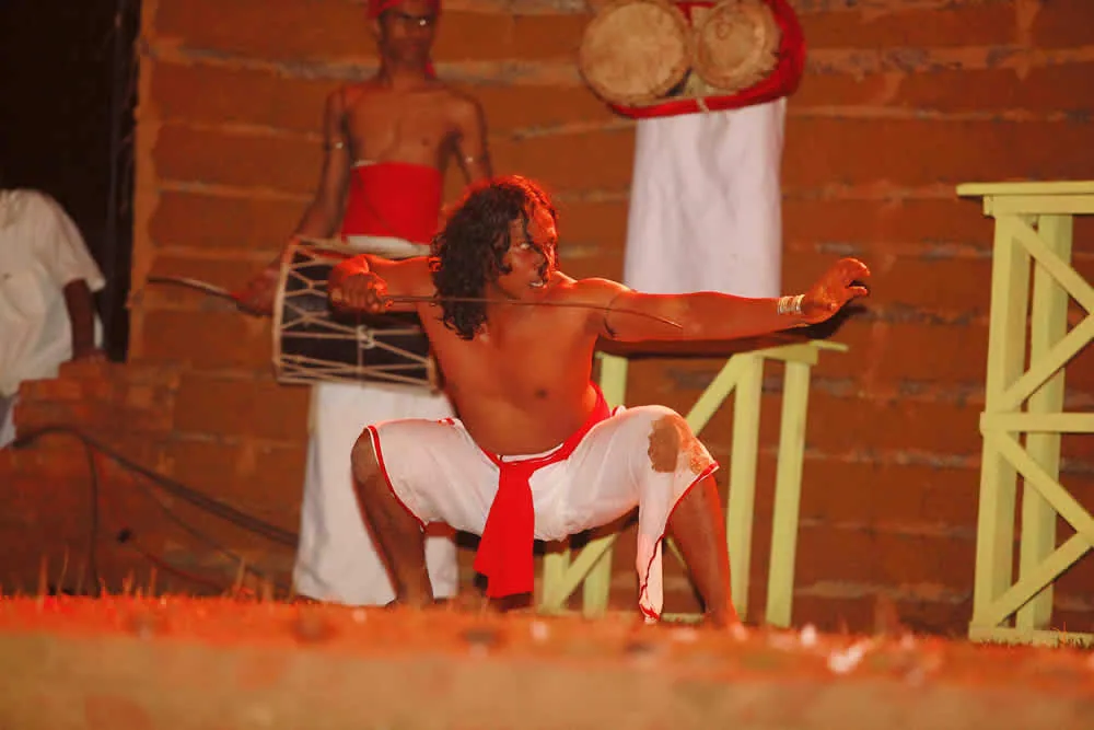 Guru Ajantha Mahantharachchi performing Angampora at a cultural event, demonstrating traditional combat stances with drummers in the background