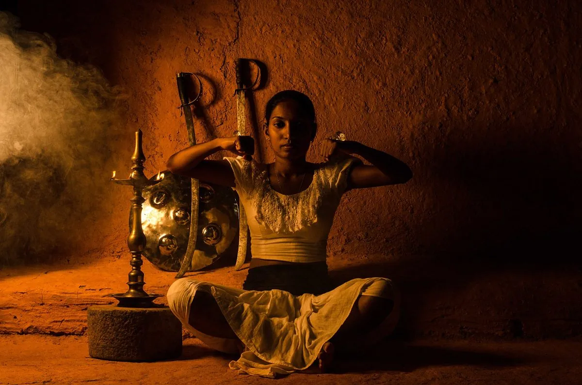 Angampora practitioner in traditional attire with shield and weapons in candlelit training hall, Sri Lanka