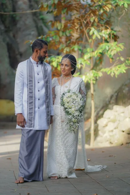 A Sri Lankan couple in traditional Kandyan wedding attire celebrating their outdoor ceremony surrounded by tropical nature - the kind of authentic backdrop that draws Indian couples to Sri Lanka