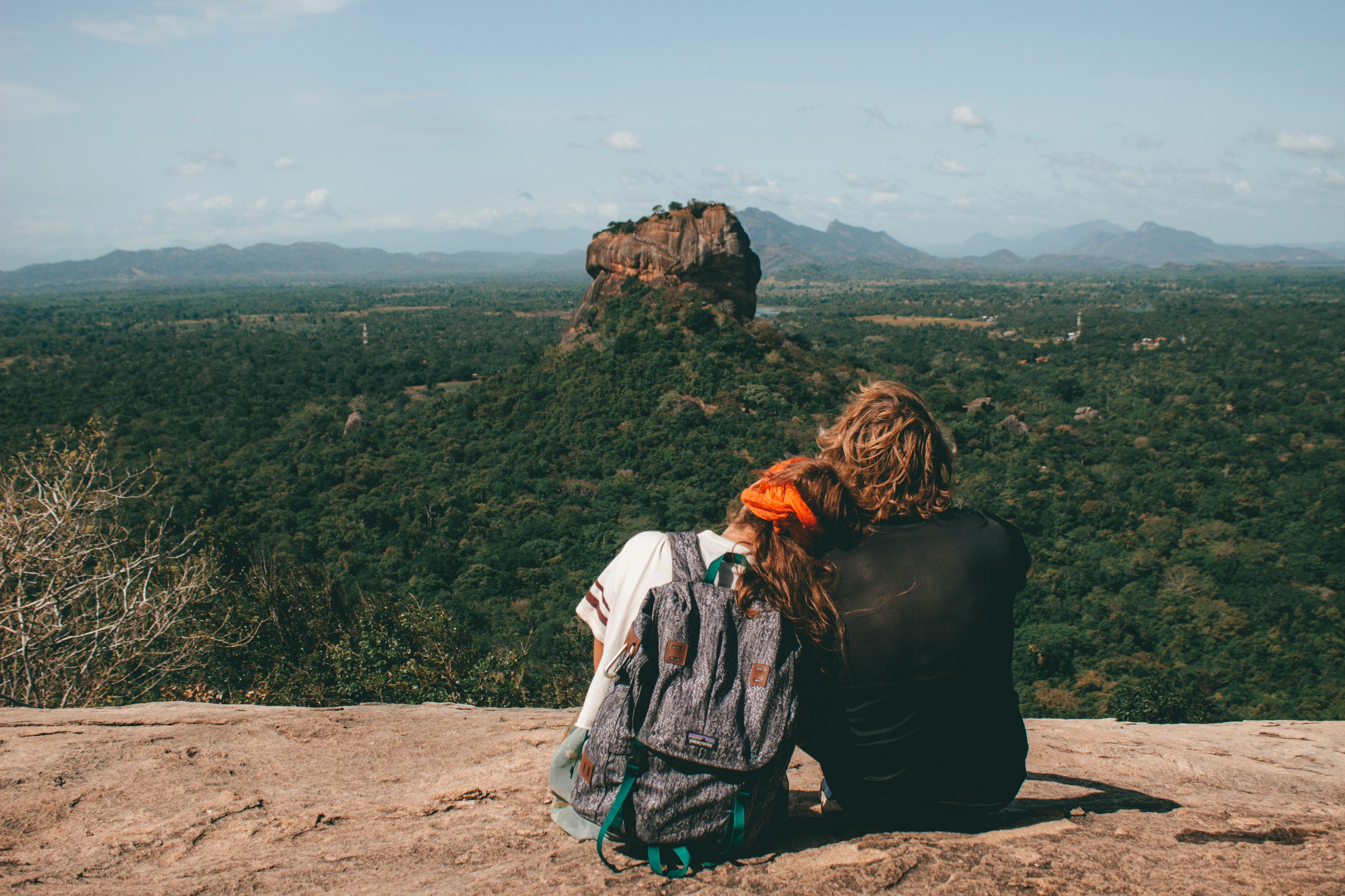A couple sitting together on Pidurangala Rock looking across the jungle canopy at Sigiriya Rock Fortress, Sri Lanka