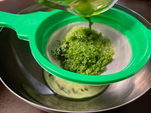 Stirring freshly strained green herb juice into the coconut milk rice porridge to make Kola Kanda