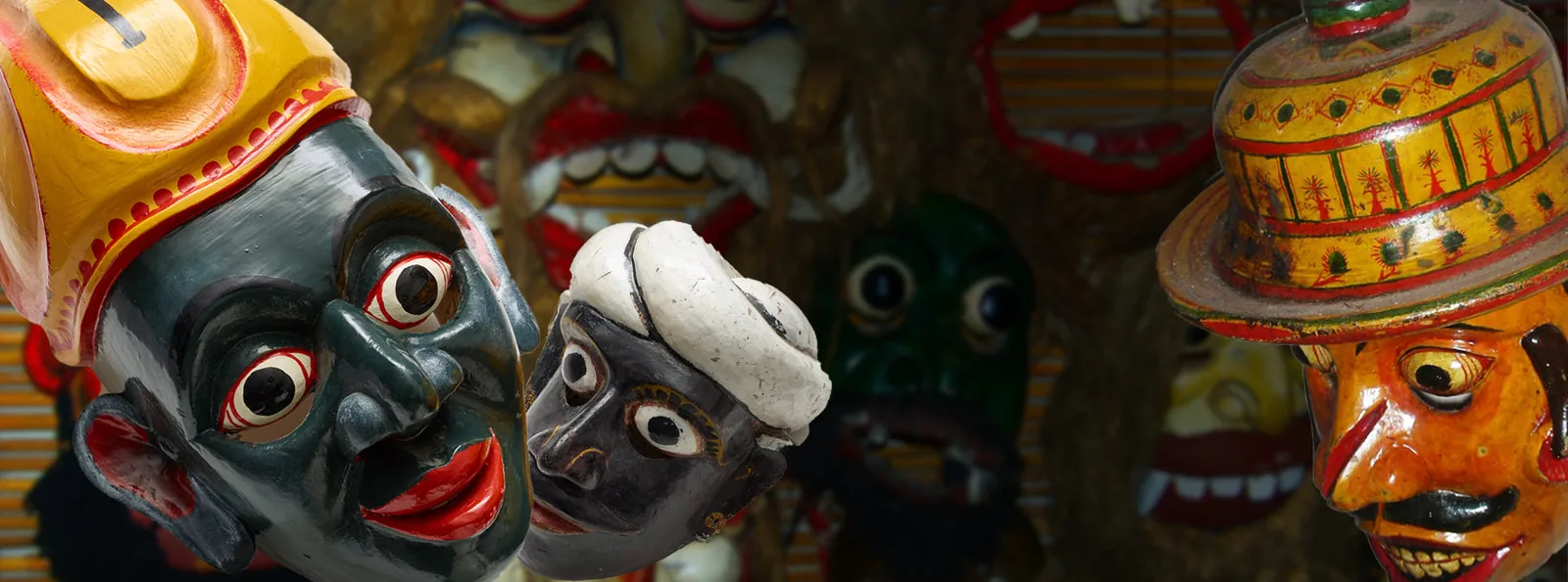 A brightly painted Kolam mask from Sri Lanka depicting a human character in vivid red, gold and green, used in traditional dance-drama performances