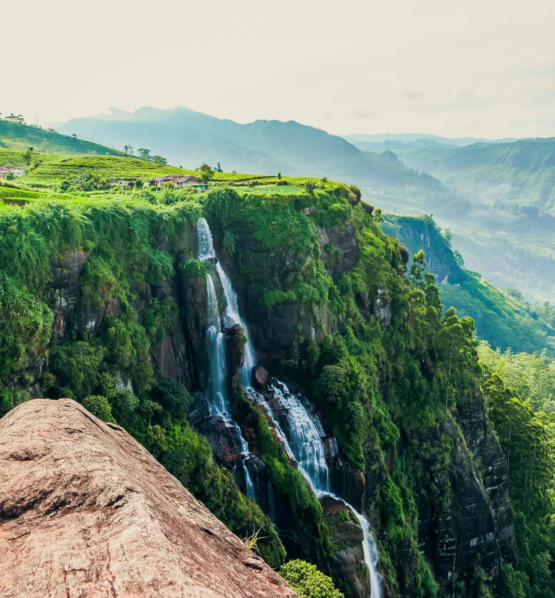 Green valley and mountain views from a viewpoint above Ella, Sri Lanka, with mist rolling through the hills and tea estates in the foreground