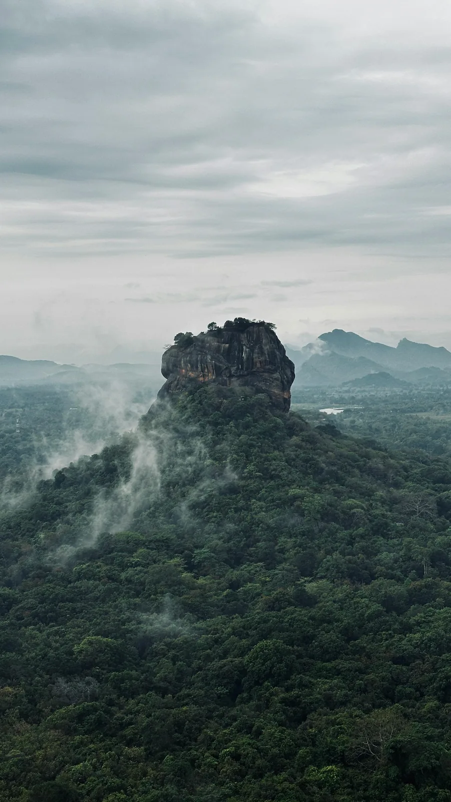 Panoramic view from Pidurangala Rock summit at sunrise showing Sigiriya Rock rising above the jungle with mist in the valley