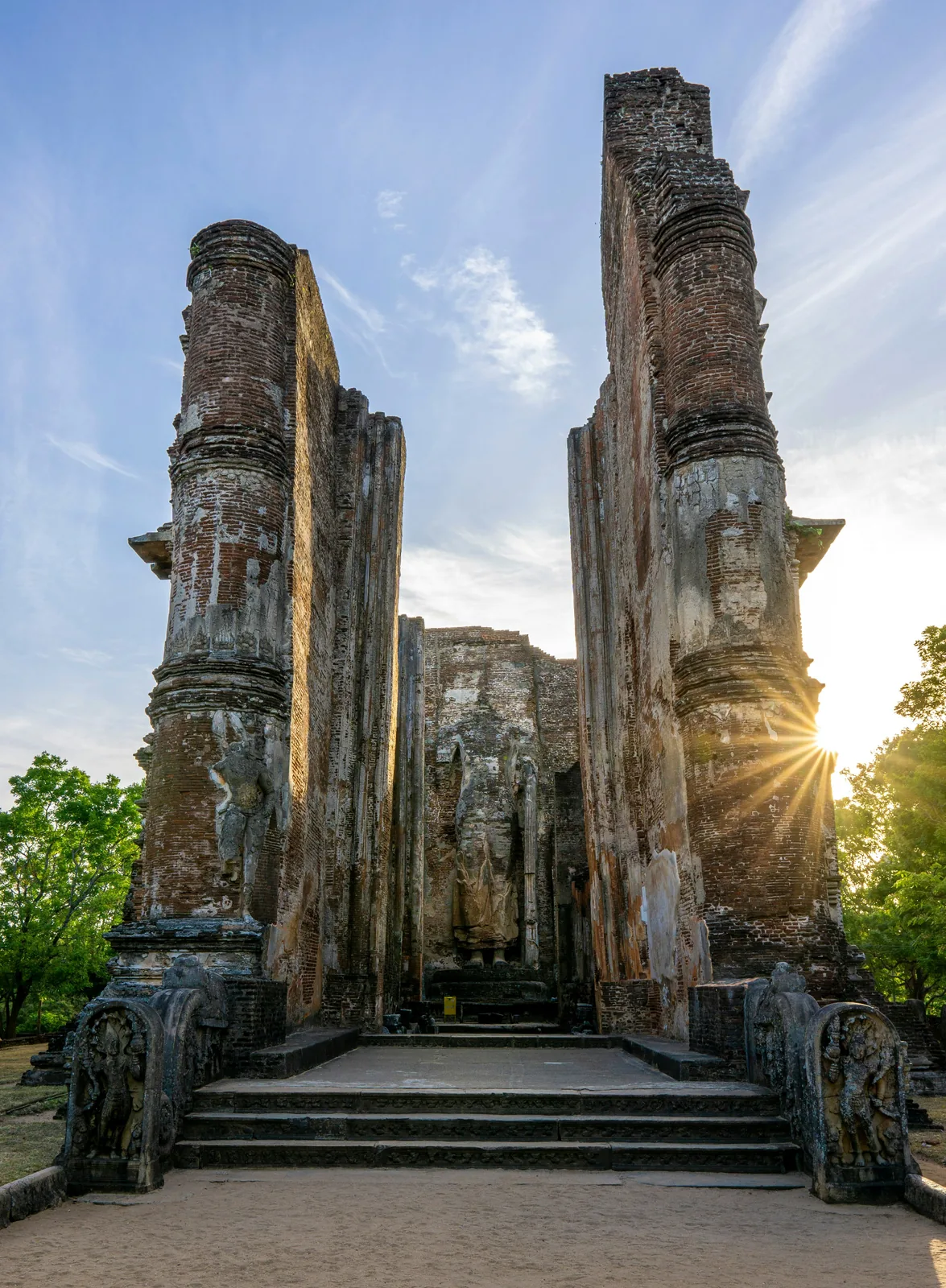 Tall ancient brick columns of Lankatilaka temple at sunset in Polonnaruwa, with a sunstar bursting between the towering walls