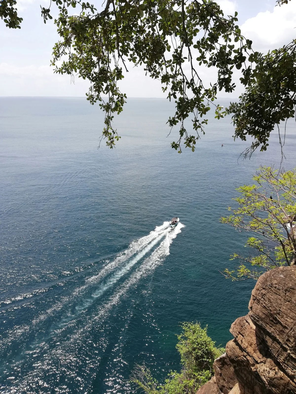 View from Swami Rock cliff at Koneswaram Temple looking down at deep blue ocean with a small speedboat leaving a white wake, Trincomalee