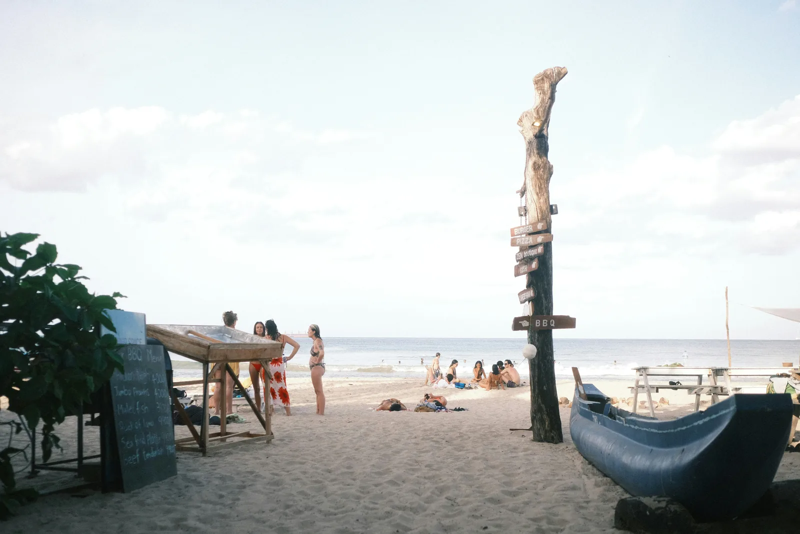 Beach restaurant and bar at Uppuveli with a BBQ signpost, people relaxing on white sand, and the Indian Ocean in the background