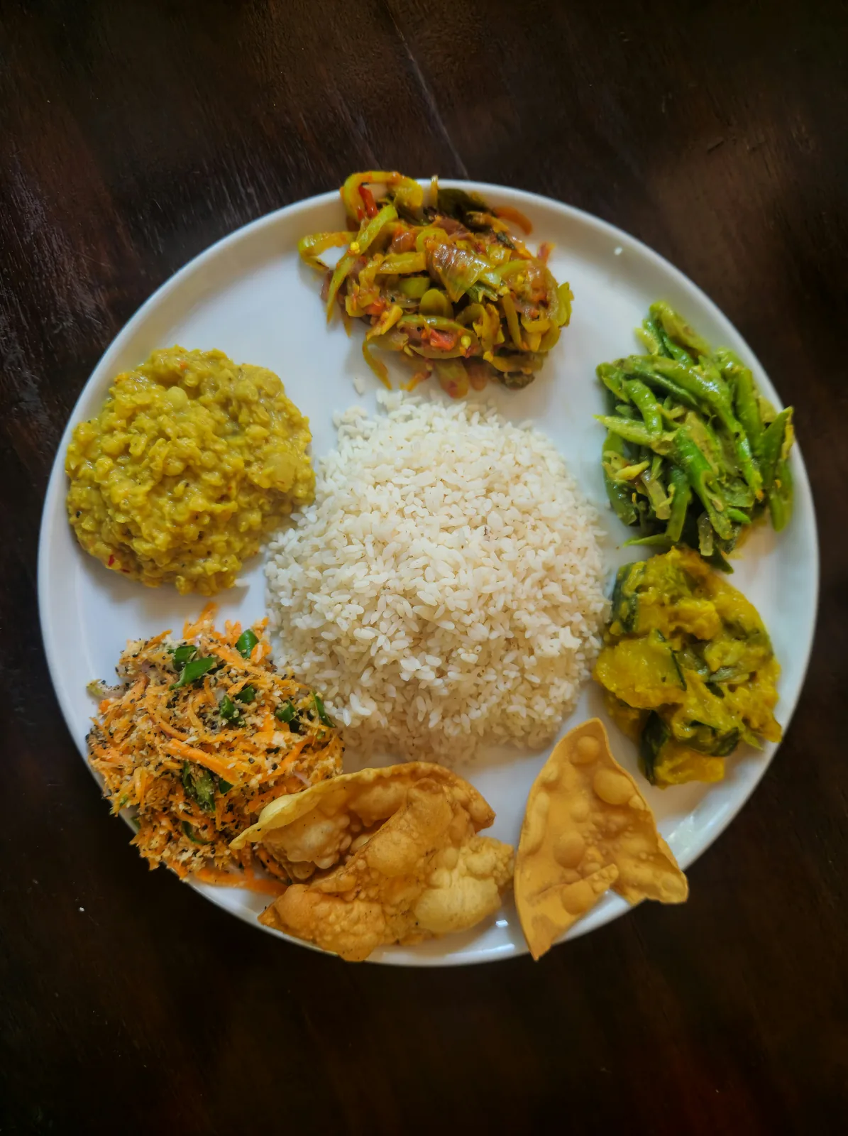 A Sri Lankan rice and curry plate with dhal, green beans, mallung and papadam arranged around the rice